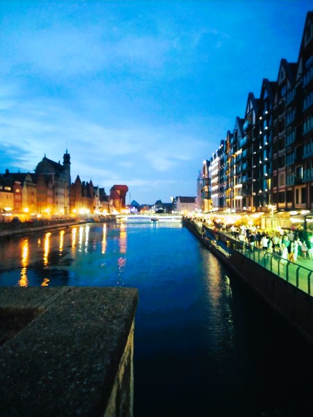 Näkymä Gdańskin Green Bridgeltä joelle illalla. Talot reunustavat jokea, paljon ihmisiä kadulla.